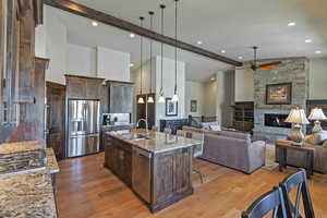 Kitchen featuring light stone counters, hanging light fixtures, a kitchen island with sink, dark brown cabinets, and beam ceiling