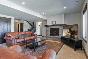Living room featuring light colored carpet, a stone fireplace, stairway, and recessed lighting