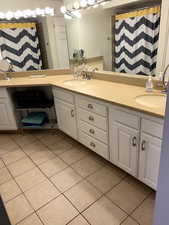 Bathroom featuring double vanity, a shower with curtain, and light tile patterned floors