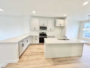Kitchen featuring stainless steel appliances, light wood finished floors, and white cabinetry