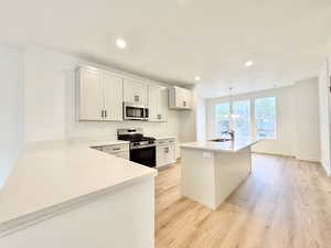 Kitchen featuring stainless steel appliances, light wood-style flooring, light stone counters, an island with sink, and pendant lighting