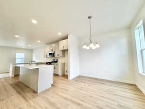 Kitchen featuring light wood-style floors, white cabinetry, an island with sink, and stainless steel appliances