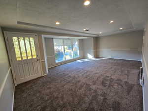 Empty room featuring a tray ceiling, recessed lighting, dark carpet, and a textured ceiling