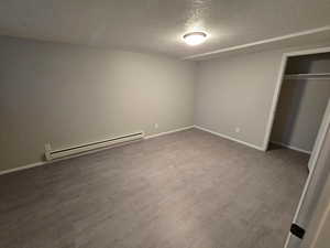 Unfurnished bedroom featuring a textured ceiling, a baseboard radiator, light wood finished floors, and a closet