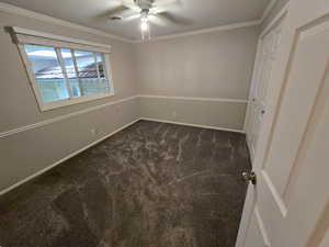 Spare room featuring ornamental molding, dark colored carpet, and a ceiling fan
