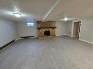 Basement with a textured ceiling, a stone fireplace, light wood-style flooring, and wooden walls
