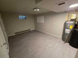 Basement featuring baseboard heating, water heater, light wood-style flooring, and a textured ceiling
