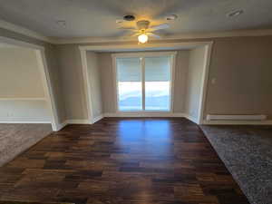 Empty room with dark colored carpet, ornamental molding, a ceiling fan, a textured ceiling, and baseboard heating