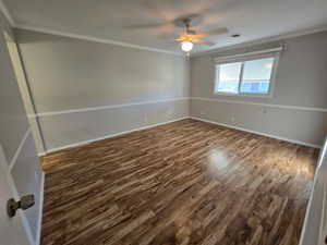 Spare room with dark wood-style flooring, crown molding, and a ceiling fan