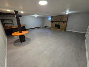 Basement featuring a stone fireplace, light wood-style flooring, a textured ceiling, and wooden walls
