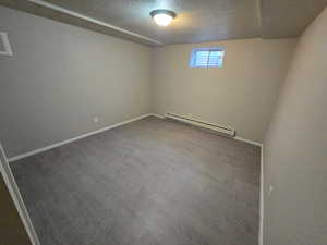 Unfurnished room featuring a textured ceiling, a baseboard radiator, and wood finished floors