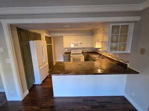 Kitchen with white appliances, a peninsula, recessed lighting, dark wood finished floors, and white cabinets