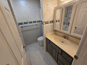 Full bathroom with wallpapered walls, vanity, light tile patterned floors, tile walls, and a wainscoted wall