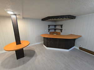 Indoor dry bar featuring a textured ceiling, light countertops, open shelves, and light wood-style floors