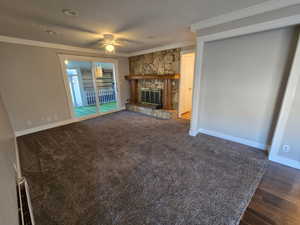 Unfurnished living room featuring crown molding, a stone fireplace, a ceiling fan, and a textured ceiling