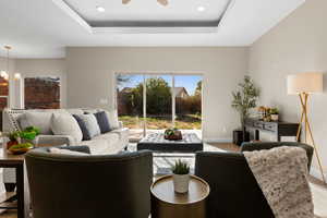 Living room featuring wood finished floors, a ceiling fan, a raised ceiling, and hanging lights