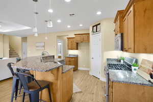 Kitchen with stainless steel appliances, dark stone counters, pendant lighting, wood finish cabinets, and a kitchen breakfast bar