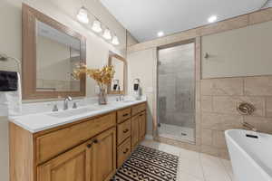 Bathroom with a soaking tub, light tile patterned floors, double vanity, a stall shower, and tile walls