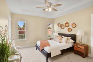 Carpeted bedroom featuring a tray ceiling and a ceiling fan