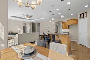 Dining space featuring a ceiling fan, light wood-type flooring, hanging lights, and a raised ceiling