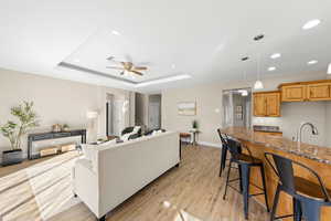 Living room with ceiling fan, light wood-type flooring, recessed lighting, and a tray ceiling