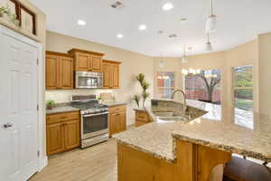 Kitchen with stainless steel appliances, a chandelier, light wood-style floors, light stone countertops, and a large island with sink
