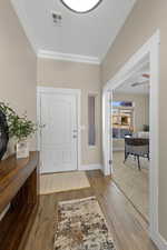 Entryway featuring light wood-style flooring, crown molding, and light carpet