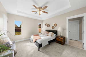 Carpeted bedroom featuring a ceiling fan and a raised ceiling