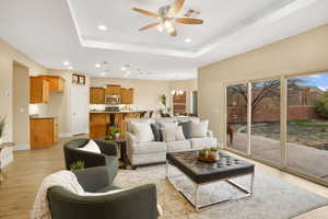 Living room with light wood-style flooring, ceiling fan, a tray ceiling, and a chandelier