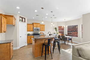 Kitchen featuring a breakfast bar, dark stone countertops, a center island with sink, light wood-style flooring, and stainless steel appliances