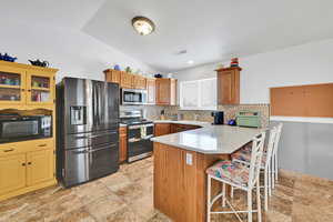 Kitchen with appliances with stainless steel finishes, a breakfast bar, a peninsula, tasteful backsplash, and glass insert cabinets