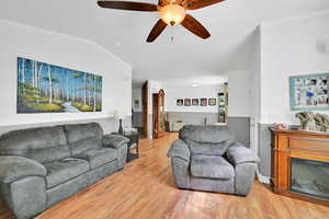 Living area with ornamental molding, a ceiling fan, wood finished floors, and a glass covered fireplace