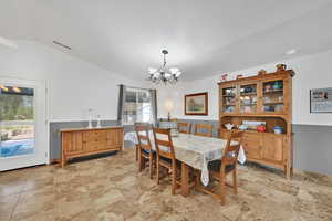 Dining room featuring a chandelier, lofted ceiling, and light stone finish floors