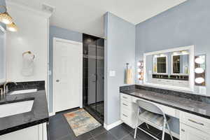 Full bath featuring double vanity, a shower stall, dark tile patterned floors, and a textured ceiling