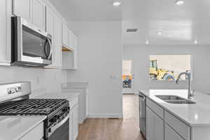 Kitchen featuring stainless steel appliances, white cabinetry, light wood-type flooring, light stone counters, and an island with sink