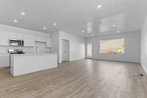 Kitchen with a kitchen island with sink, light countertops, white cabinetry, light wood-style flooring, and stainless steel appliances