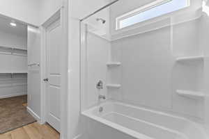 Bathroom featuring a spacious closet, shower / bath combination, and light wood finished floors