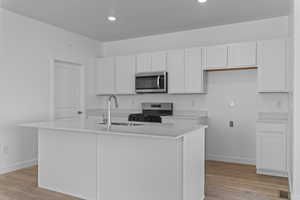 Kitchen with white cabinets, stainless steel appliances, an island with sink, and light wood finished floors