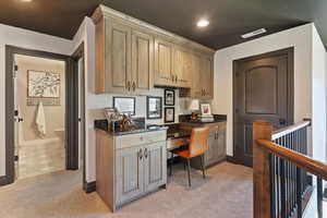 Kitchen featuring built in study area, dark stone counters, light colored carpet, and recessed lighting