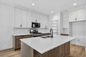 Kitchen featuring tasteful backsplash, stainless steel appliances, light wood-type flooring, a center island with sink, and two tone cabinets
