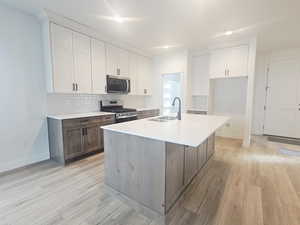 Dual tone kitchen with two tone cabinetry, stainless steel appliances, backsplash, light wood-style flooring, and an island with sink