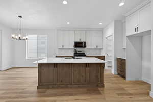 Dual tone kitchen featuring two tone cabinetry, a kitchen island with sink, suspended lighting, light stone counters, and light wood-style flooring