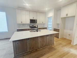 Two tone kitchen featuring dual tone cabinets, light wood-type flooring, stainless steel appliances, backsplash, and a kitchen island with sink
