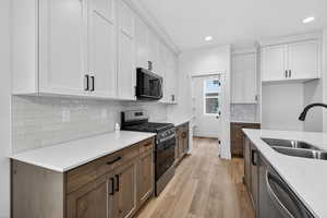 Dual tone kitchen with two tone color scheme, stainless steel appliances, light wood-style flooring, light stone counters, and recessed lighting