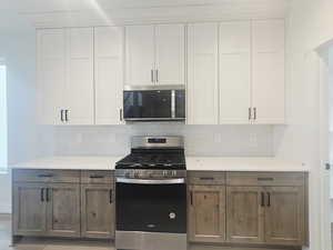 Dual tone kitchen with stainless steel appliances, dual tone cabinets, decorative backsplash, and light stone counters