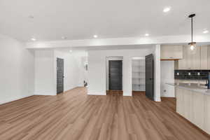 Kitchen featuring pendant lighting, light wood finish cabinets, modern cabinets, light wood-type flooring, and decorative backsplash