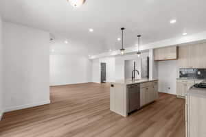 Kitchen with open floor plan, pendant lighting, stainless steel dishwasher, light stone countertops, and light wood-style floors