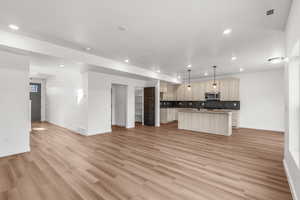 Kitchen with open floor plan, an island with sink, decorative light fixtures, backsplash, and light countertops