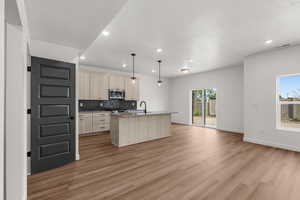 Kitchen featuring pendant lighting, open floor plan, an island with sink, light wood finish cabinets, and light wood-style floors