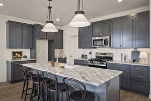 Kitchen with a kitchen bar, stainless steel appliances, light stone counters, and dark wood finished floors